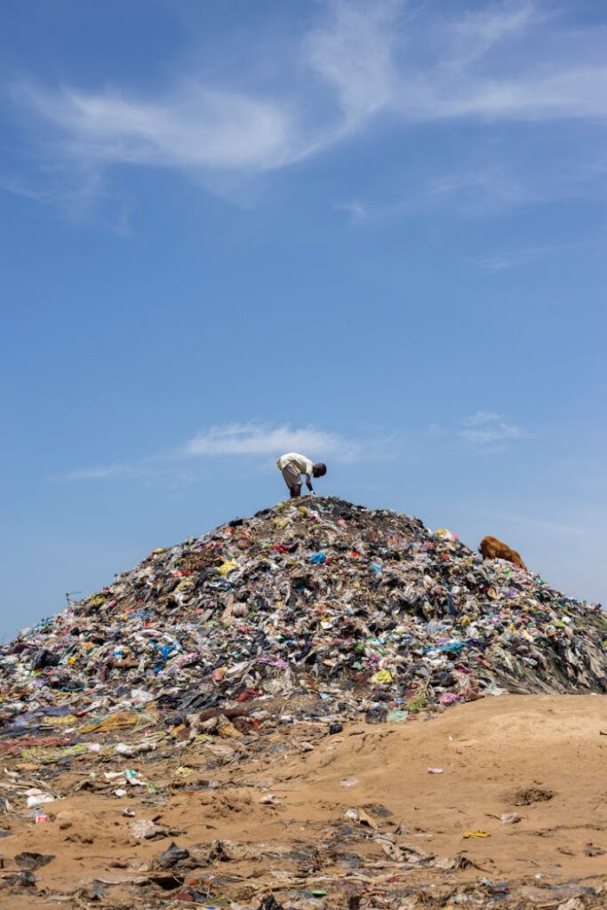 pexels photo 25851683 A man stands atop a mound of garbage under a bright blue sky, highlighting pollution.